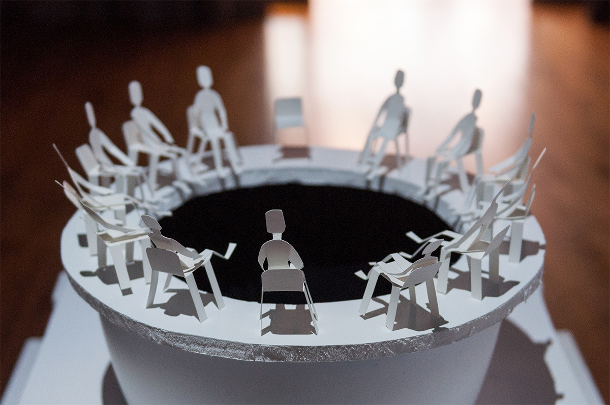 A mini circular put surrounded by paper chairs and paper people sitting in them