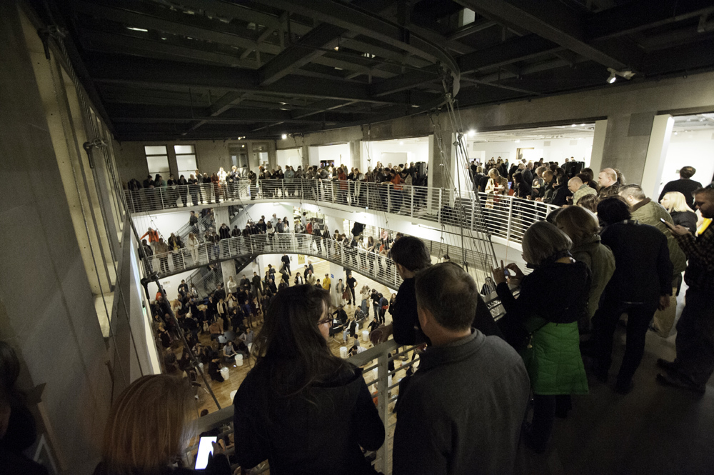 Crowds of people gathered at the railings of the contemporary atrium structure during a First Thursday performance at Pacific Northwest College of Art (PNCA). 
