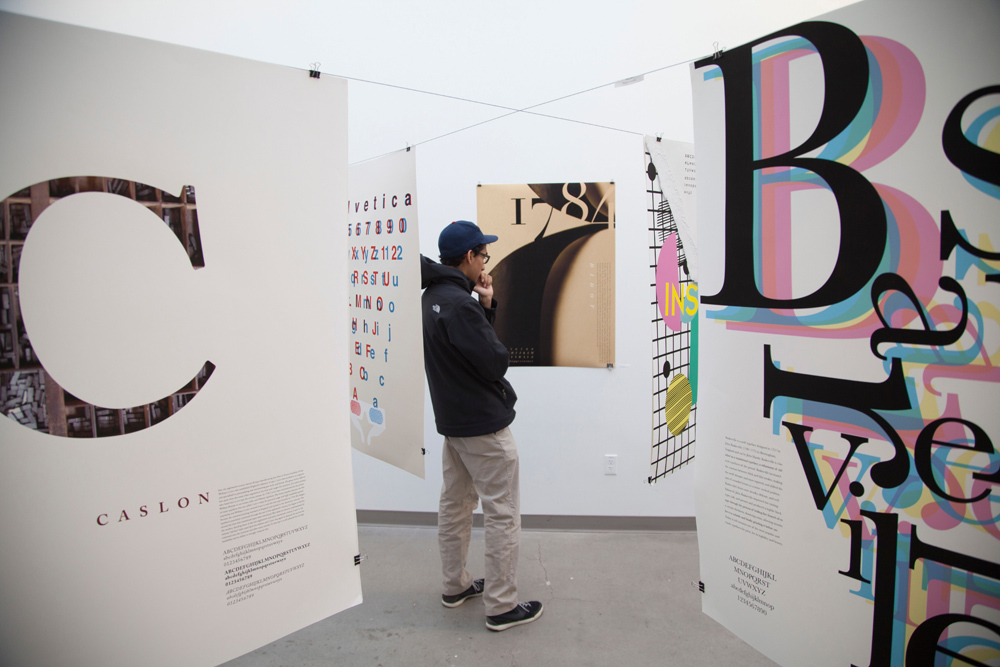 Person standing among posters hanging in Typecasted, Pacific Northwest College of Art (PNCA)'s Design Student Poster Expo, Feb. 2016. 