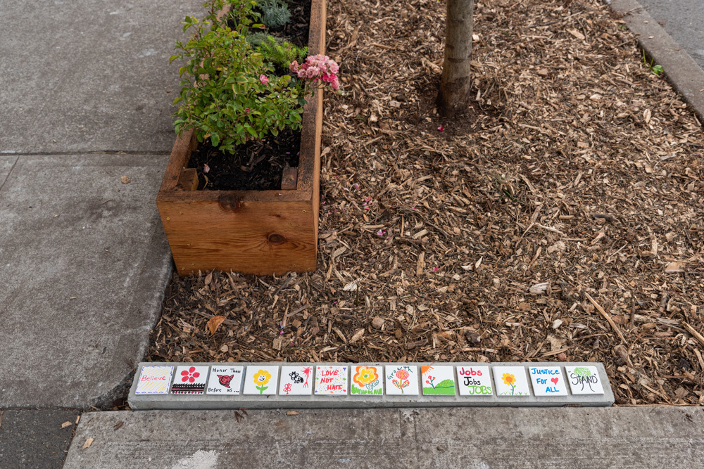 A planter on bark dust near a set of inspirational tile artwork lined up in a row