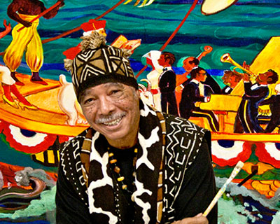 Pacific Northwest College of Art (PNCA) Alumni and Professor Emeritus Arvie Smith posing in front of one of his brightly colored and energetic paintings.