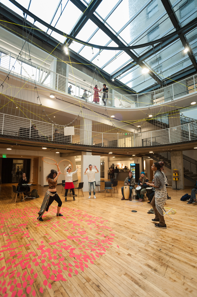 Pacific Northwest College of Art (PNCA) students and alumni gathered in an open wood floored area playing drums and hula hooping during a 2015 Focus Week performance.