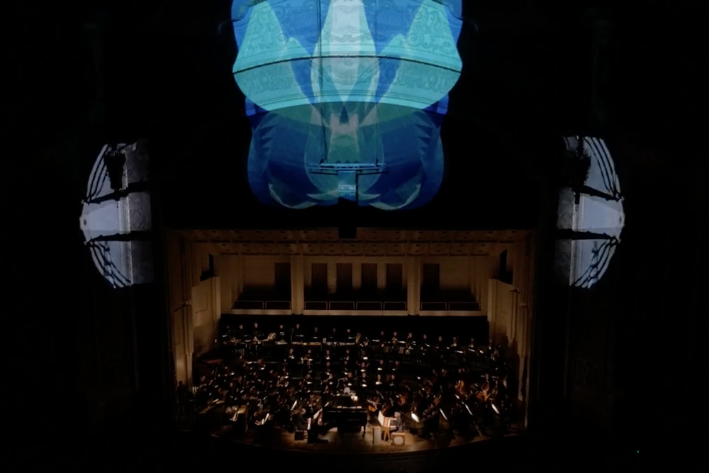 2016 Oregon Symphony performing in a darkened Arlene Schnitzer Concert Hall in downtown Portland, Oregon with the stage lit up by colorful projection mapped images created by Rose Bond and PNCA students.