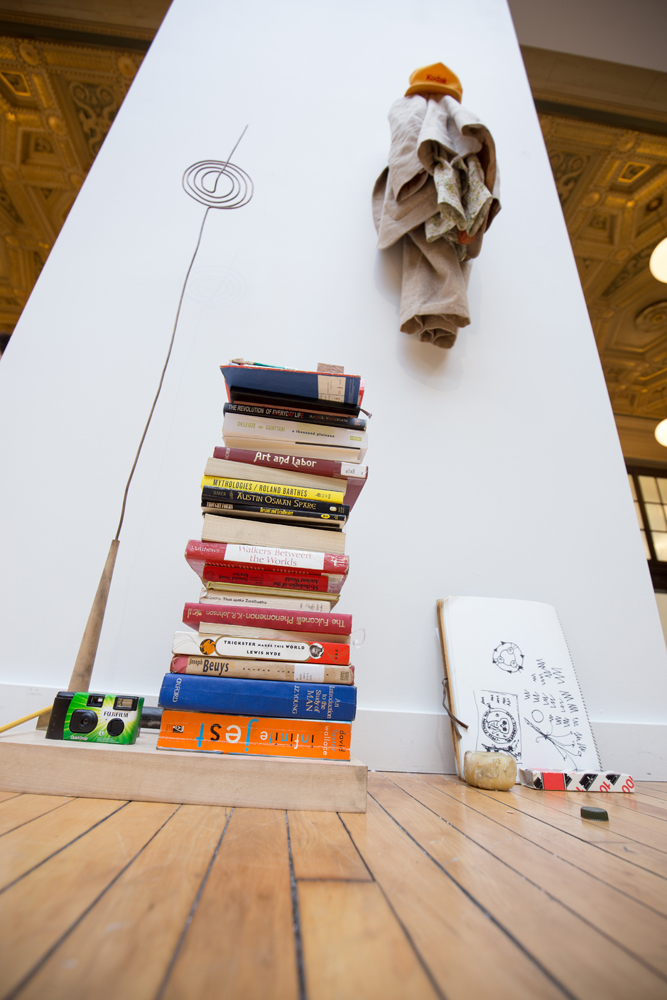 A stack of books next to a camera, drawing, hat, and other goods