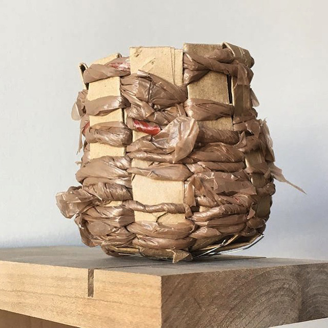 A sculpture made out of wood and plastic brown bags that forms a bowl