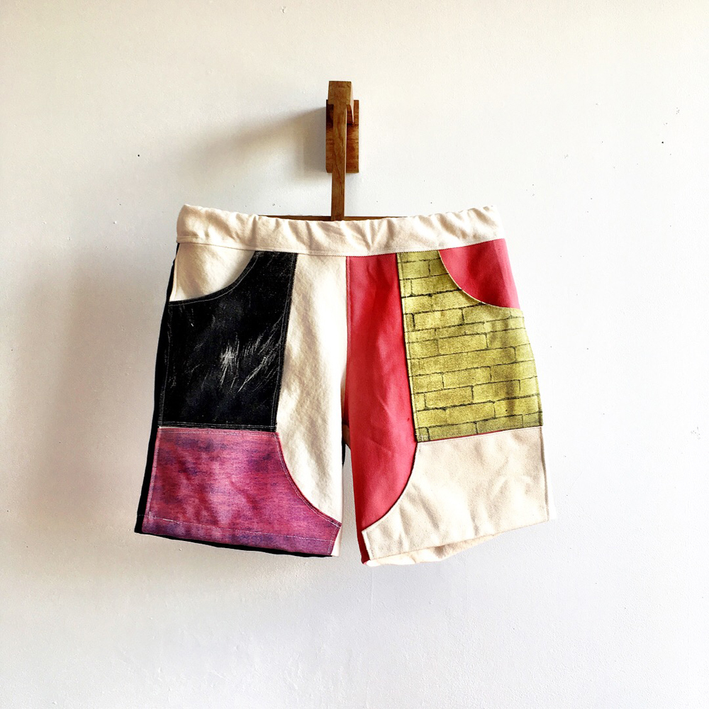 A hanging pair of shorts using a geometric design with white, black, red, purple, and gold