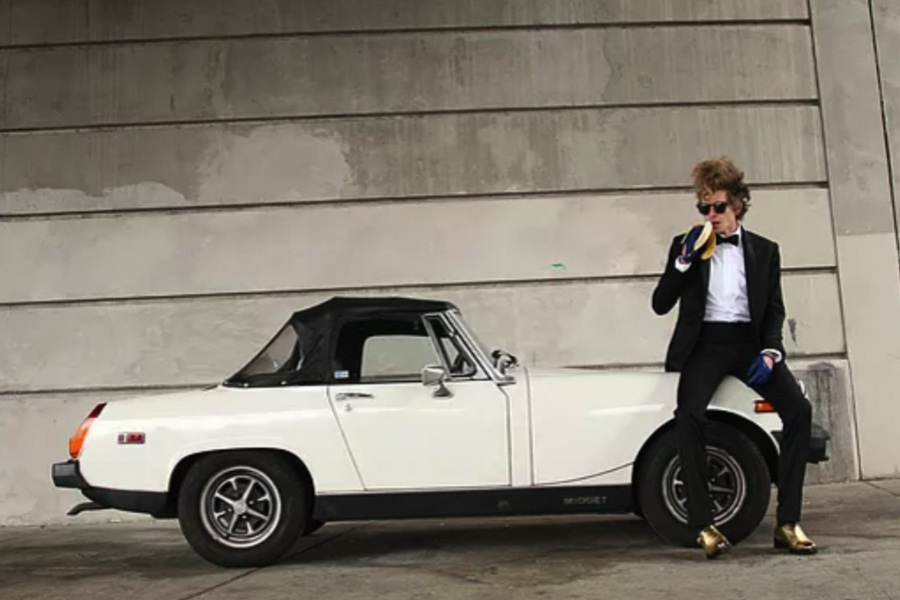 Adam Arnold in a tuxedo sitting on top of a retro white car