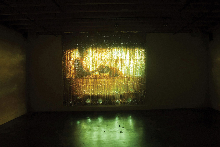 Demian Dineyazhi's exhibition featuring a person taking a path projected on a gold screen
