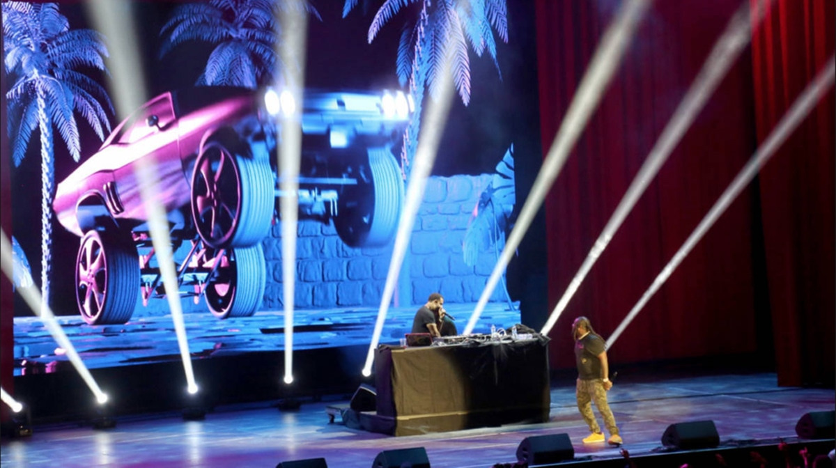 T-Pain performance with a background visual of a car with large extended wheels in the air